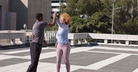 Friends celebrating post-workout high-five on sunlit urban rooftop terrace
