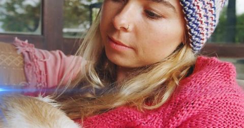 Woman in knit beanie and cozy sweater holding puppy by window