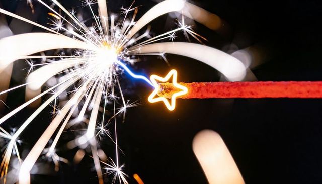 Close-up sparkler star tip igniting with radiant sparks and blue arc, macro bokeh