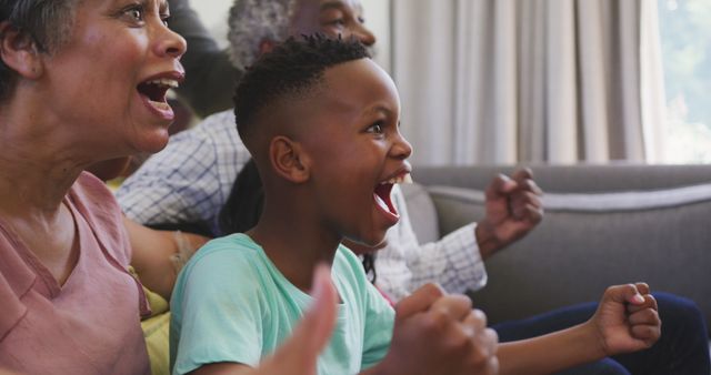 Three generations of a black family displaying excitement and joy as they watch TV in the living room. Perfect for use in content related to family bonding, happy moments, or home entertainment.