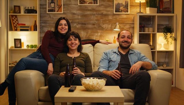 Three friends relaxing on couch with beer and popcorn in cozy living room