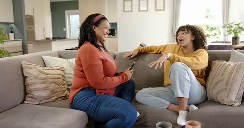 Friends Chatting on Sofa in Cozy Living Room Holding Smartphone