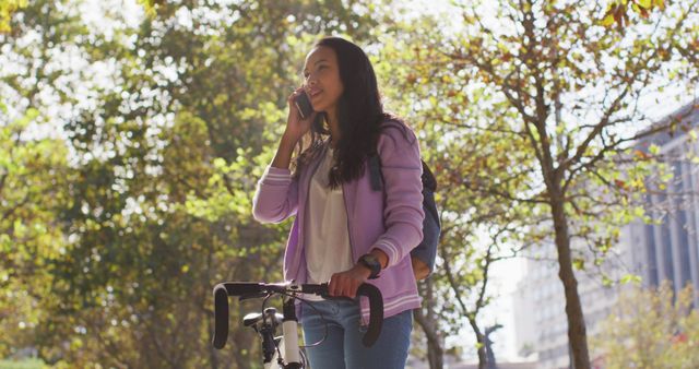Asian woman with bicycle smiling talking on smartphone while standing in the park. modern lifestyle and living concept