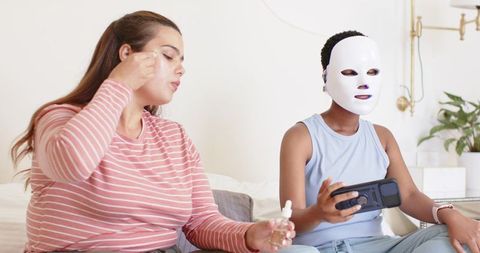 Two friends enjoying skincare routine with led mask and facial serum at home