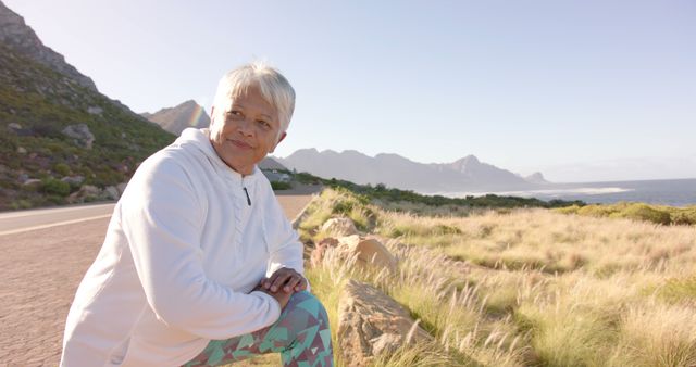 Senior woman enjoying a serene moment during outdoor exercise amidst beautiful mountain scenery. This image is ideal for promoting healthy lifestyles, retirement activities, fitness, and mental well-being. Perfect for use in travel brochures, health and wellness campaigns, and inspirational content.