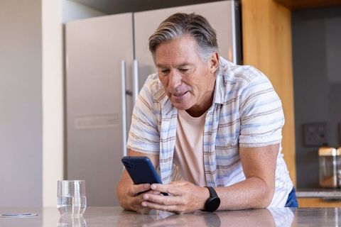 Senior man checking smartphone while leaning on kitchen counter casual home technology