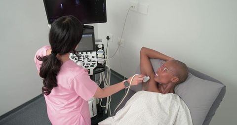 Female sonographer performing diagnostic ultrasound on patient lying on exam bed in clinic