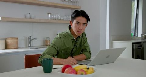 Focused Young Man Working from Home with Laptop and Notepad