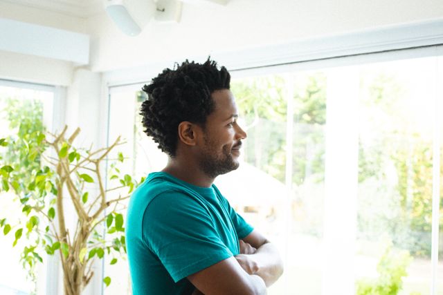 Smiling african american young man looking away while standing with arms crossed at home. unaltered, lifestyle, leisure activity and domestic life concept.