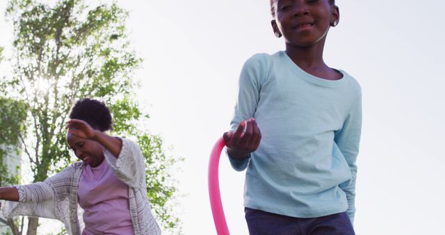 Image of happy african american granddaughter and grandmother using hula hoops in park, copy space. Health, free time, togetherness, family and inclusivity.