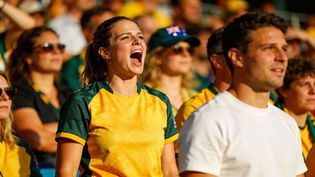 Enthusiastic female fan cheering loudly in yellow-green jersey in sunny stadium stands