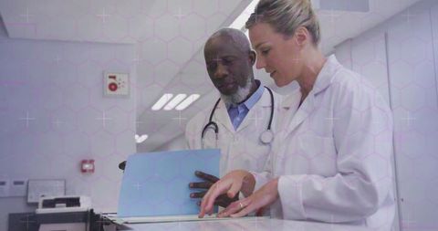 Doctors collaborating on patient records in hospital corridor reviewing medical documentation