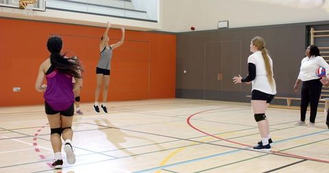 Diverse female volleyball team practicing jump serve and team drills in school gymnasium