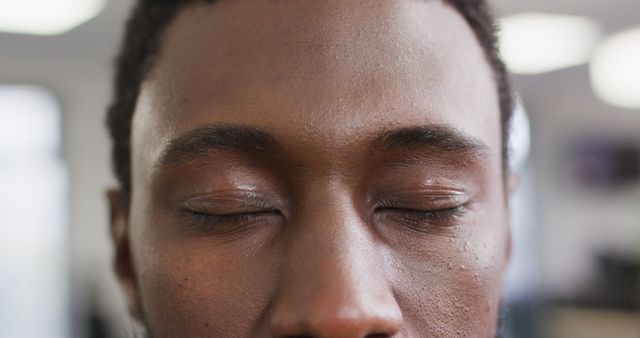 Depicts an African American man with eyes closed in a peaceful state, emphasizing meditation and relaxation. Can be used for articles, blogs, promotional materials focusing on mental health, wellness, and mindfulness practices.