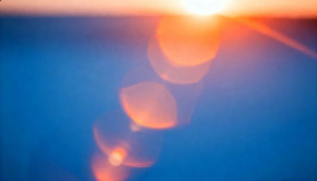 Sunrise lens flare scattering warm orange bokeh over tranquil blue seascape horizon