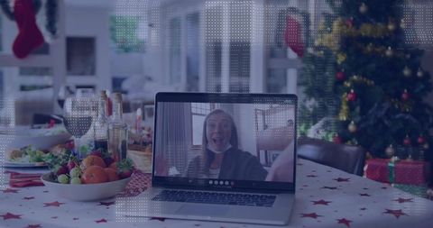 Waving woman on laptop during virtual holiday dinner with christmas tree and gifts