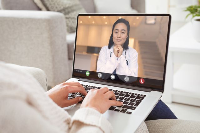 Caucasian woman using technology for an online medical consultation with an Asian female doctor. Ideal for articles about telemedicine, healthcare technology, remote medical services, and the impact of telehealth on patient care. Suitable for illustrating concepts of modern healthcare, virtual consultations, and connecting with healthcare professionals from home.