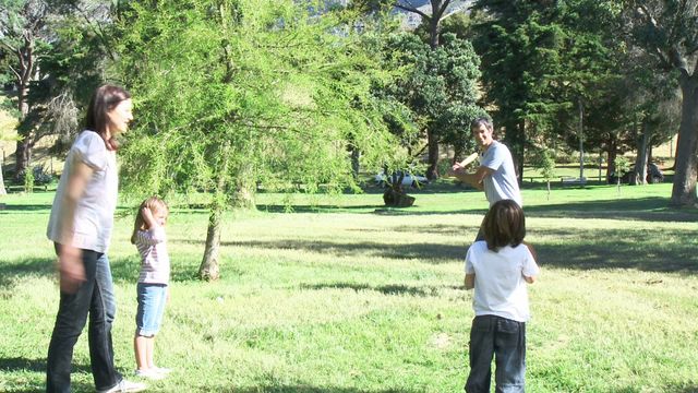 Parents and children playing an informal game of baseball in a lush park on a sunny day. Perfect for illustrating family outdoor activities, bonding moments, recreational sports, and lifestyle concepts.