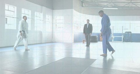 Gi Fighters Walking to Center Mat While Referee Observing in Bright Martial Arts Gym