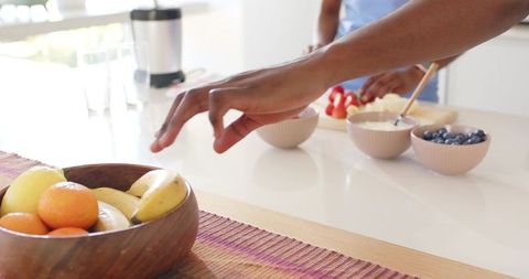 Friends reaching for wooden fruit bowl while preparing colorful breakfast bowls
