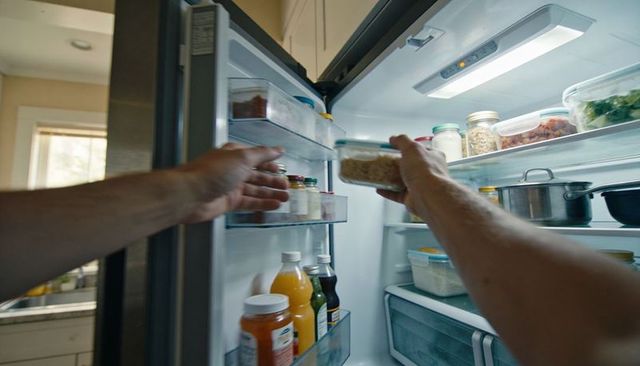 Male arms reaching into stainless-steel fridge grabbing grain container in bright kitchen