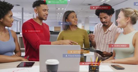 Diverse team collaborating around laptop in open office with social media notifications
