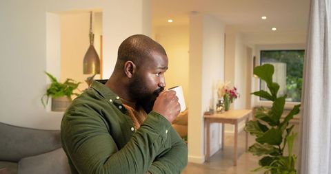 African American man sipping coffee, enjoying calm morning among living room plants