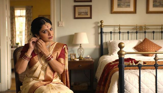 Bridal woman adjusting gold jewelry wearing cream silk sari and red blouse