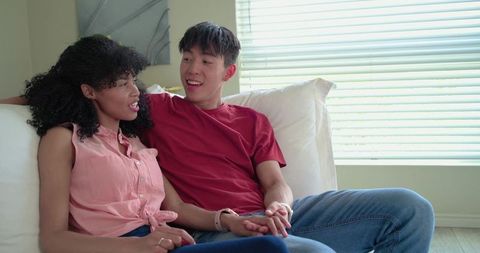 Asian man and african american woman holding hands on couch, sharing warm conversation