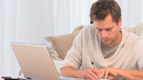 Man Concentrating on Calculating Bills with Laptop at Home