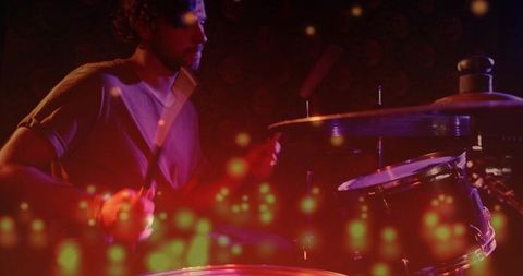 Male drummer playing live drum kit with colorful bokeh and moody stage lighting