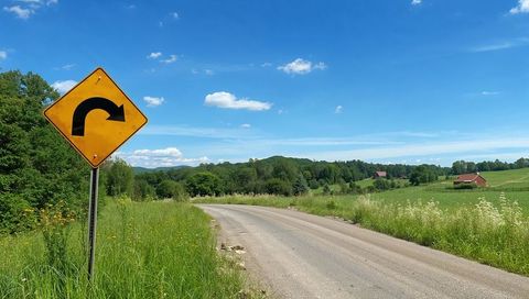 Yellow right turn sign pointing along winding country lane under blue summer sky