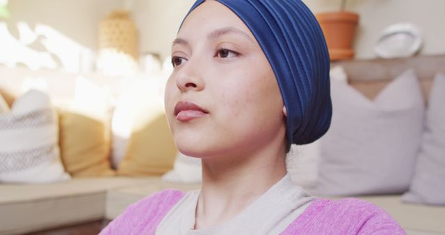 Image of tranquil biracial woman in hijab doing yoga meditation, closing eyes and deep breathing. Happiness, health, fitness, inclusivity and domestic life.