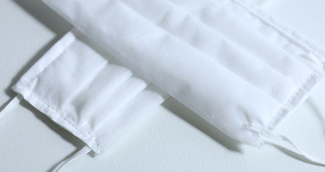 Closeup image of white fabric face masks placed on a light surface. Ideal for articles, advertisements, and educational materials focusing on hygiene, health safety measures, and protective gear. Can be used by healthcare organizations, wellness blogs, and online stores selling protective face masks.