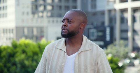African american man gazing left on urban plaza wearing beige striped shirt and white tee