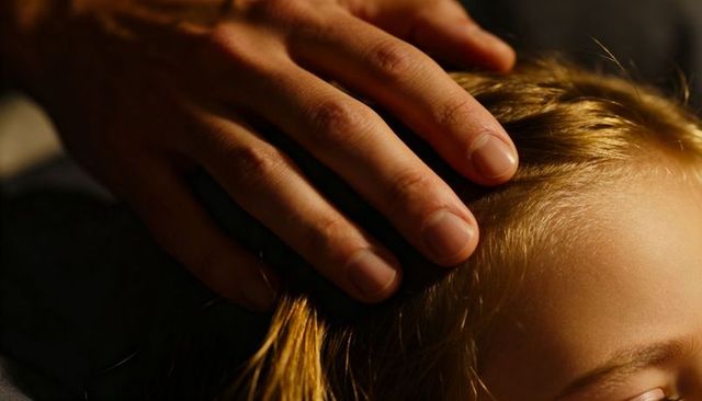 Gentle adult hand cradling blonde child's hair conveying tenderness and family bonding