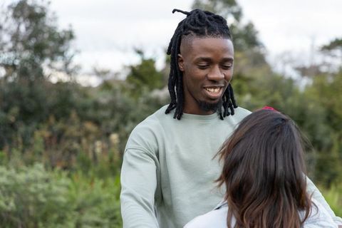 Black man smiling and chatting with partner in park greenery casual candid connection