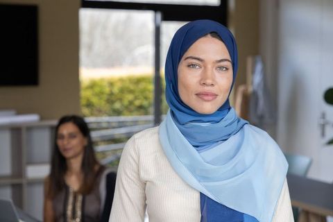 Confident woman wearing blue hijab standing in modern office workspace