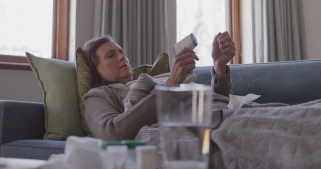 Senior woman lying on sofa, holding a medicine bottle. This can be used in health, recovery, and medication related topics. Ideal for blogs or articles on senior health care, home recovery and the importance of regular medication.