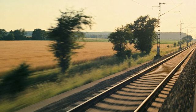 Gliding sunlit railway through golden farmland at sunset with motion blur and catenary