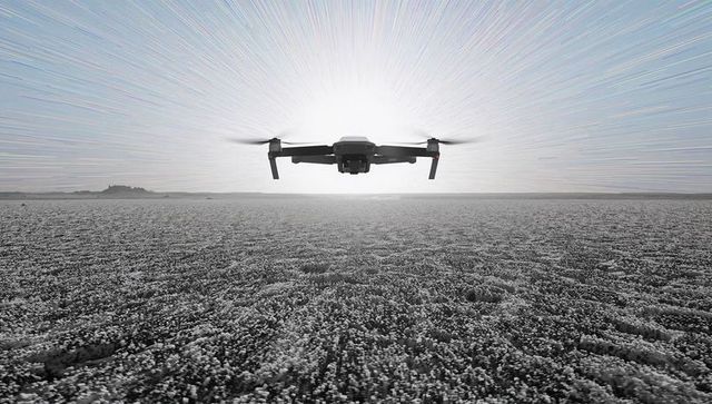 Backlit quadcopter hovering over salt flat with sun halo and radial light streaks