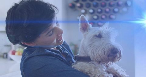 Smiling woman holding white terrier in bright kitchen with warm sunlight and lens flare