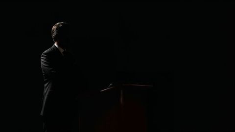 Silhouette of Speaker on Dark Stage Delivering Speech