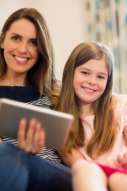 Portrait of mother and daughter using digital tablet in living room at home