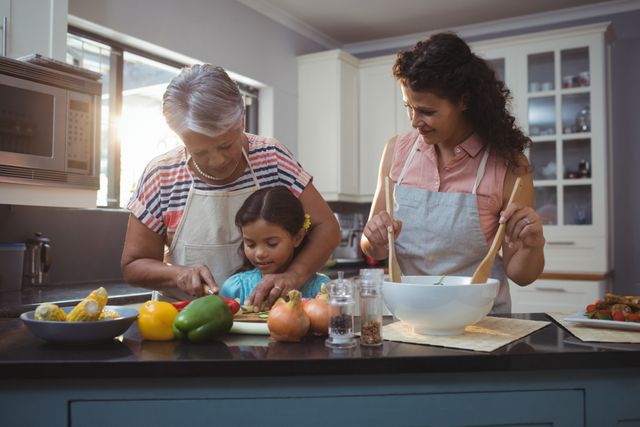 Grandmother teaching granddaughter to chop vegetables in kitchen, with mother assisting. Ideal for use in family-oriented content, cooking tutorials, healthy eating promotions, and advertisements focusing on family bonding and multigenerational activities.