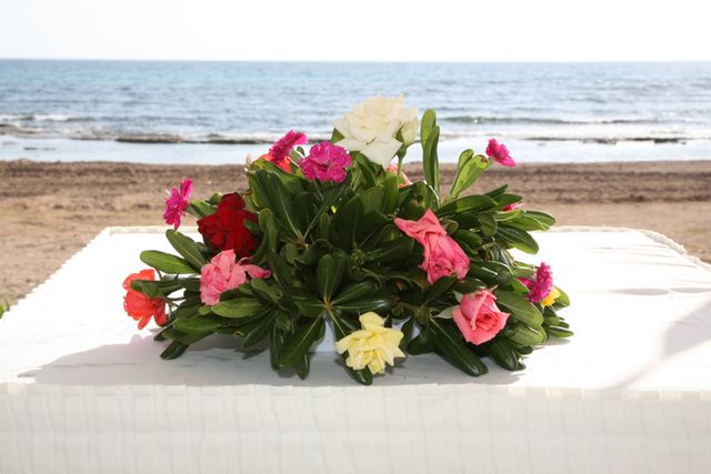 Colorful floral arrangement with various flowers on a white table beside a beach. Suitable for use in wedding promotions, vacation brochures, romantic getaways, event planning, and nature-themed designs.