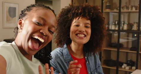 Diverse friends laughing and waving during casual selfie in cozy kitchen with glass jars