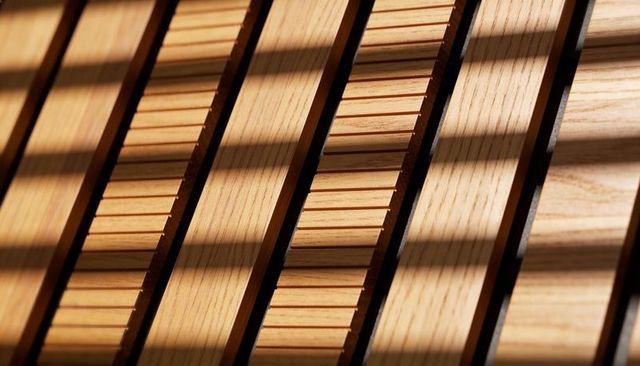 Sunlit oak slats casting diagonal shadows across grooved wooden paneling texture
