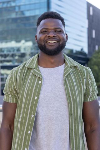 Confident african man smiling outdoors on urban plaza wearing green striped shirt