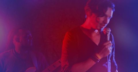 Male Vocalist Singing Holding Mic on Moody Backlit Stage with Guitar Silhouette Haze